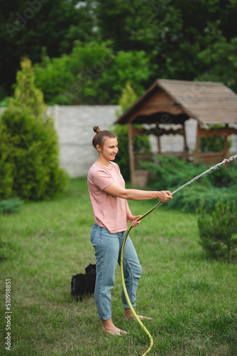 Attractive young girl is watering the lawn with a hose