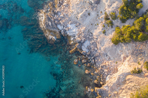 Aerial top down view of waves crashing against rocks in turquoise sea water © Abinieks