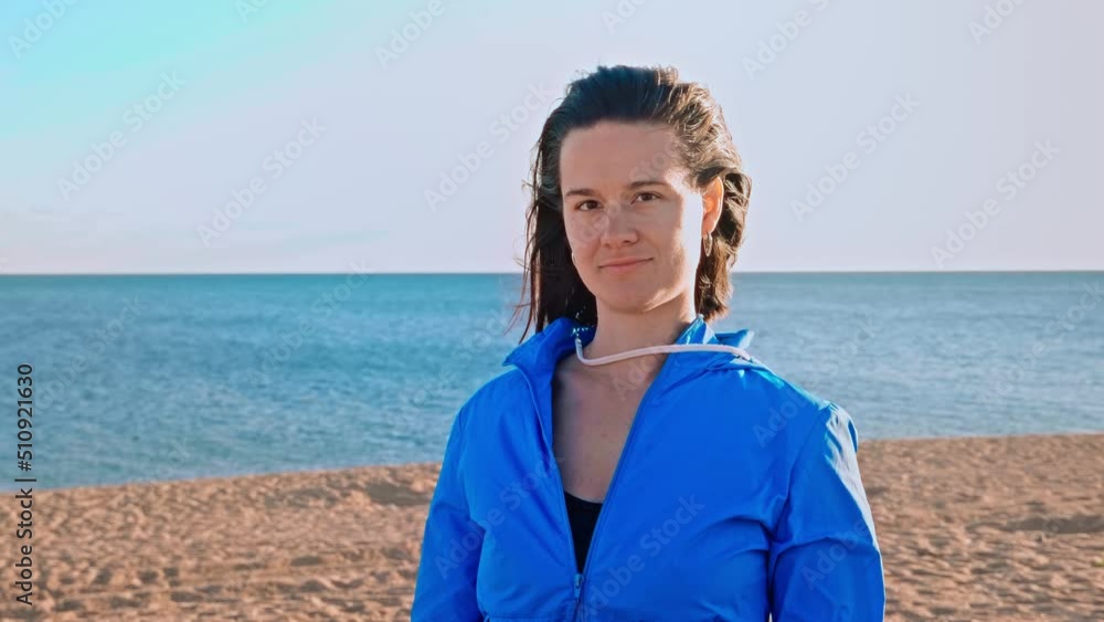 Portrait of beautiful girl on the background of clear blue sea. The girl is flirting and her hair is blowing in the wind. Happy woman in blue tracksuit against blue sky Portrait of beautiful girl on the background of clear blue sea. The girl is flirting and her hair is blowing in the wind. Happy woman in blue tracksuit against blue sky