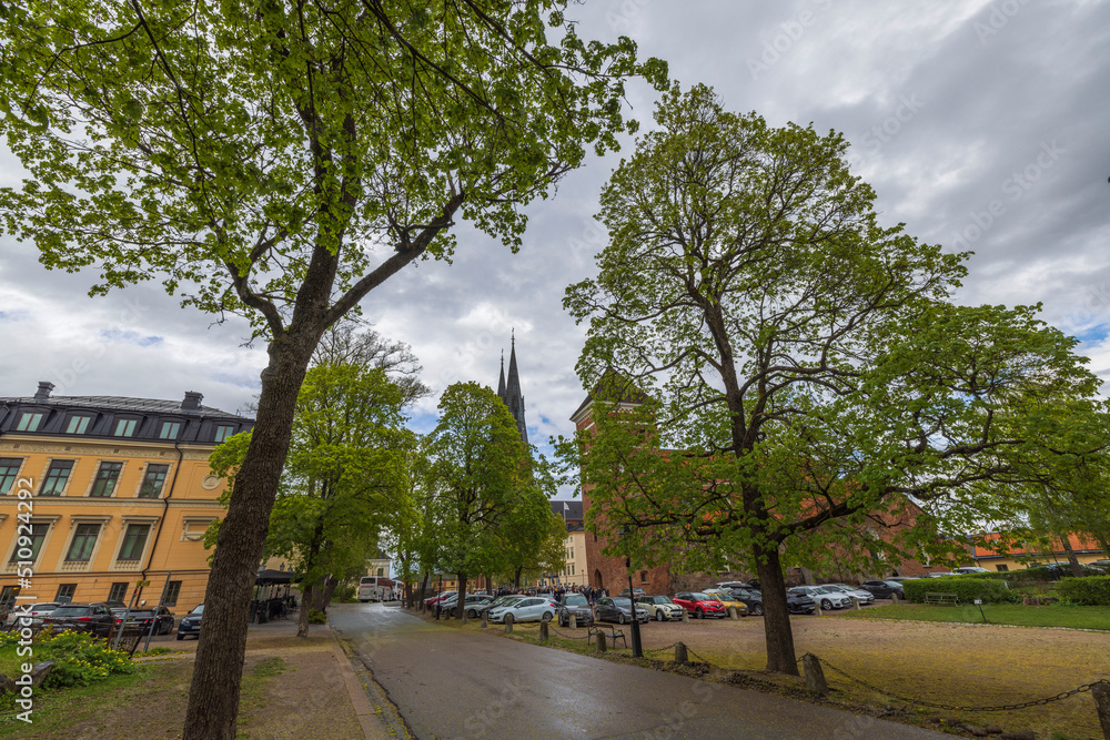 Beautiful panoramic view of empty city street with green trees and cathedral towers on background. Sweden. Uppsala.