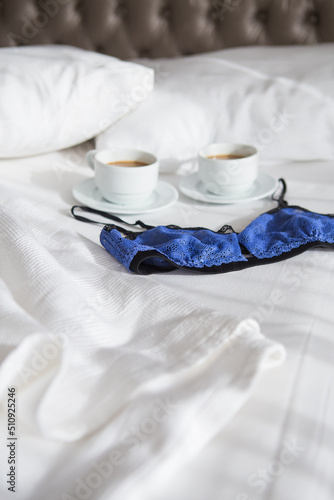 two cups of coffee and a beautiful bra on a white bed, close-up