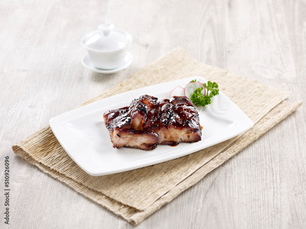 Charred BBQ Pork with Honey Sauce Served in a dish isolated on wooden board side view on grey background
