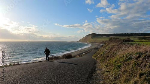 A man walking up a hill on a road on a windy afternoon along the Pacific Ocean of Whidbey Island. photo