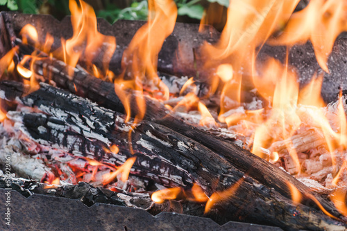Old barbecue grill with burning wood logs. Open fire from a metal box. Snack in the open air in a natural park. Logs make a fire. Bonfire smoke
