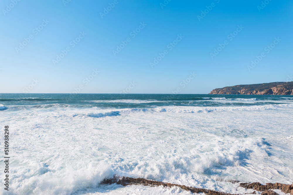 Amazing view of the Atlantic Ocean with waves, mountain and clear blue sky. Traveling in Portugal