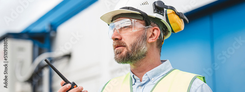 Bearded engineer wearing helmet using walkie-talkie to communicate with industry produce site. Wide imagea photo