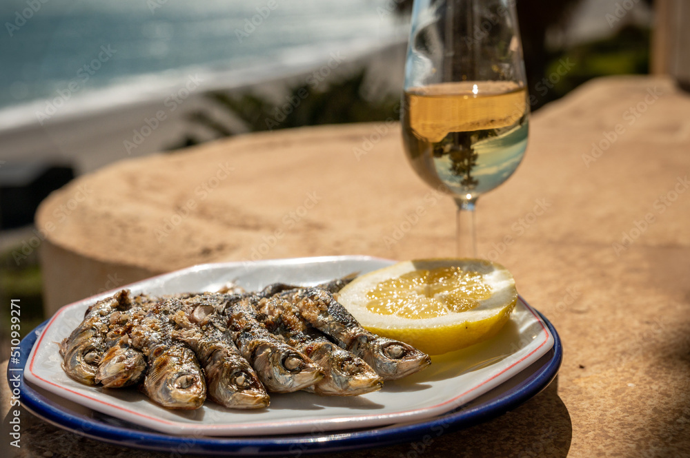 Sardines espeto prepared on skewers and open flame on fireplace with olive trees wood, served outdoor with glass of fino sherry and view on blue sea, Malaga, Andalusia, Spain