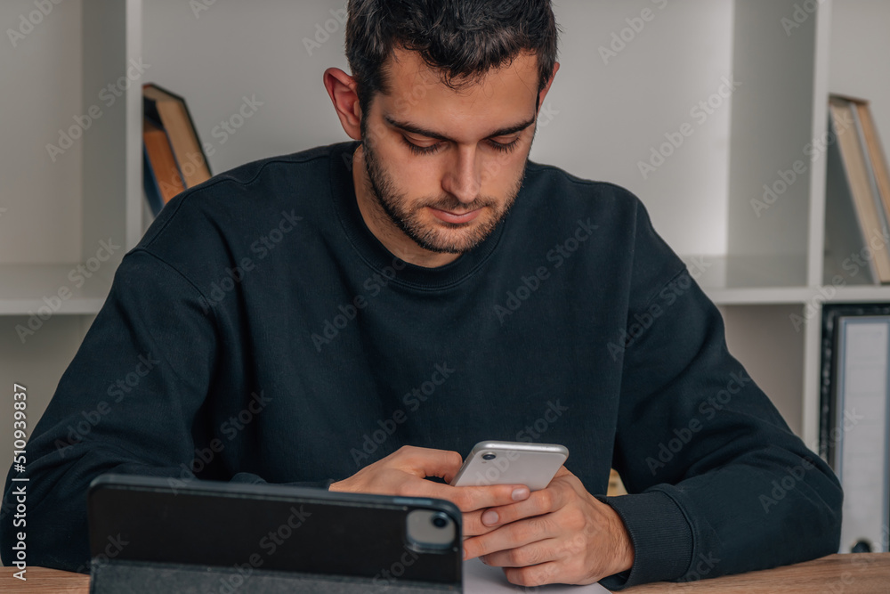 young man at desk with mobile phone and laptop or computer young man at desk with mobile phone and laptop or computer