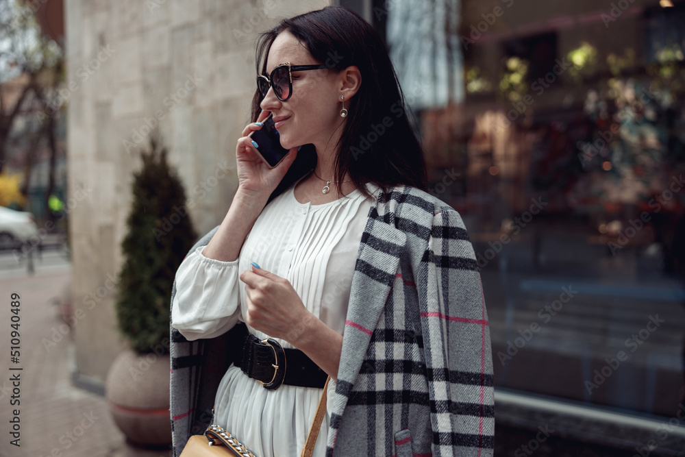 Young attractive brunette female in sunglasses talking on mobile phone at street. Young attractive brunette female in sunglasses talking on mobile phone at street.