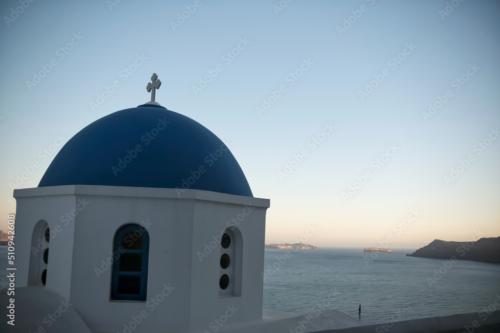 The top of a picturesque Greek Orthodox Church overlooking the Aegean Sea in Oia Santorini