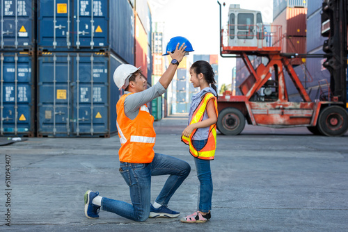 Father and little daughter wearing a safety helmet at Container cargo site. Business heir concept. Happy father and daughter wearing safety helmet work site. Business heir concept.