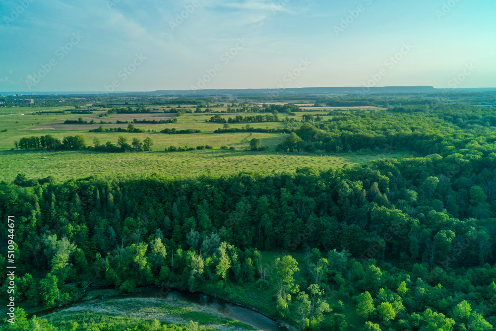Aerial shot of green fields, forests and a creek bending in the foreground