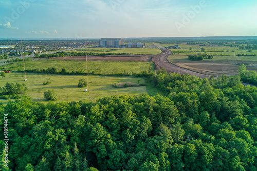 Aerial shot of Hospital in the background with dirt road construction in the middle ground and beautiful forest in the foreground