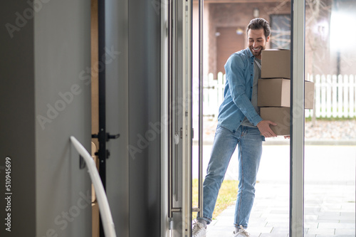 Man holding stack of boxes entering house