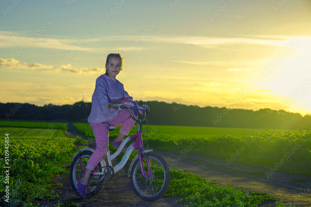 Child on a bicycle on a background of green field and with the rays of the evening sun. Child on a bicycle on a background of green field and with the rays of the evening sun.