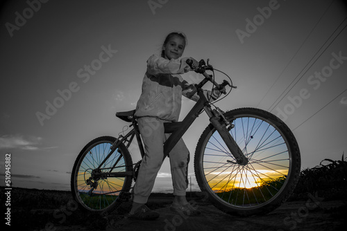 Fototapeta Naklejka Na Ścianę i Meble -  Child on a bicycle on a background of green field and with the rays of the evening sun.