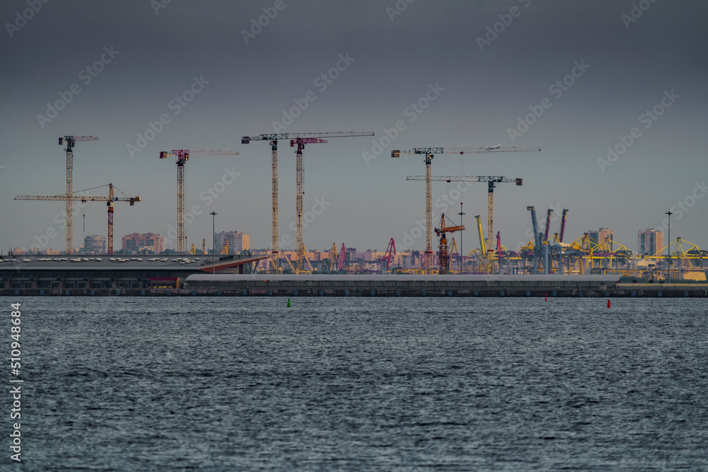 Seaport, construction cranes and cranes of the cargo port on the sea horizon in sunset light Seaport, construction cranes and cranes of the cargo port on the sea horizon in sunset light