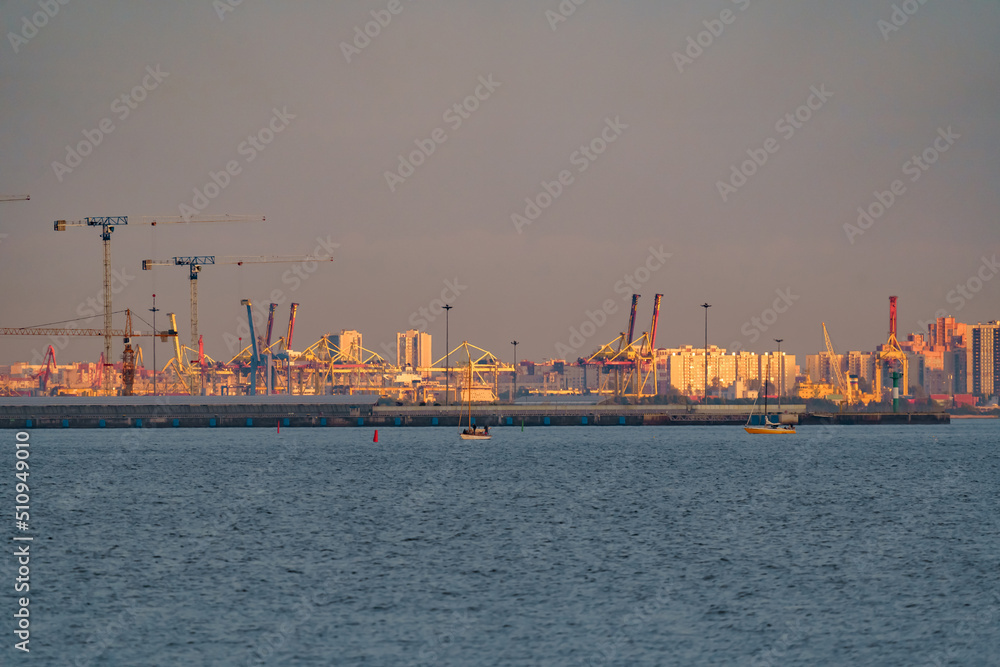 Seaport, construction cranes and cranes of the cargo port on the sea horizon in sunset light
