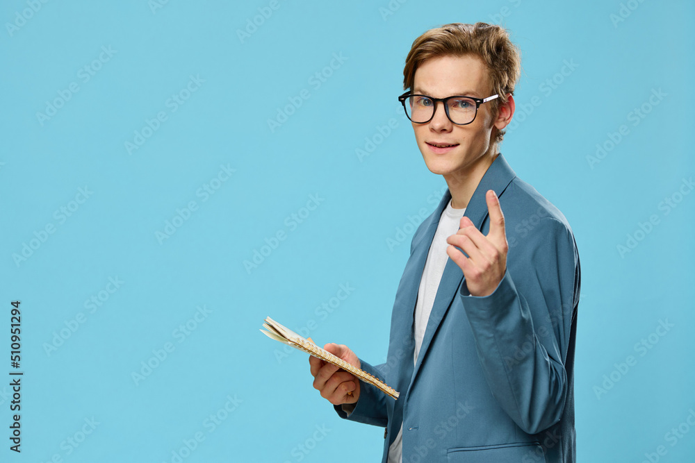 handsome funny young man stands in glasses with a notepad in his hands with a funny expression and shows his index finger up handsome funny young man stands in glasses with a notepad in his hands with a funny expression and shows his index finger up