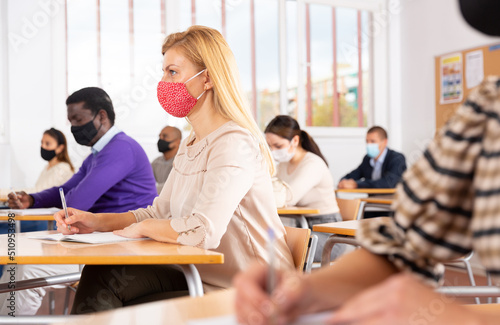 Young woman in protective face mask listening to lesson in extension school. Concept of necessary precautions and social distancing in coronavirus pandemic..