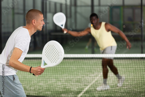 Portrait of sporty adult man playing padel on indoor court, ready to hit ball. Active lifestyle concept. © JackF