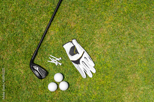 Top view of golf equipment on green grass on a golf course. Flat lay of golf club, balls, glove, tees