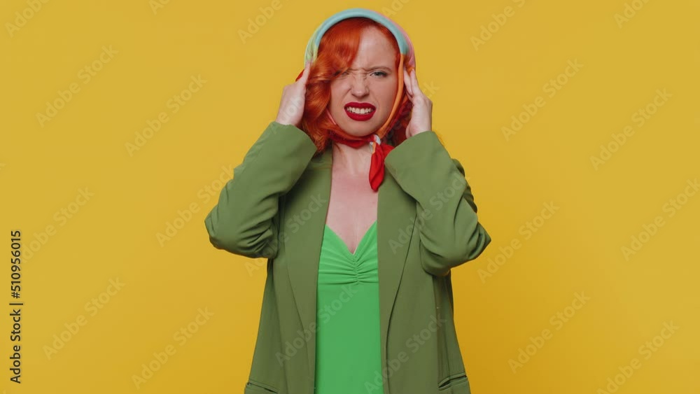 Redhead young woman in jacket rubbing temples to cure headache problem, suffering from tension and migaine, stress, grimacing in pain, high blood pressure. Girl isolated alone on yellow background Redhead young woman in jacket rubbing temples to cure headache problem, suffering from tension and migaine, stress, grimacing in pain, high blood pressure. Girl isolated alone on yellow background