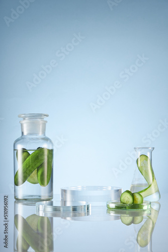 Front view of transparent podium with laboratory equipment and cucumber in blue background science content