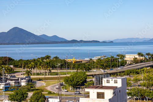 Cityscape view with road junction, ocean, mountains on the horizon, palm trees and green lawns. © Александр М.