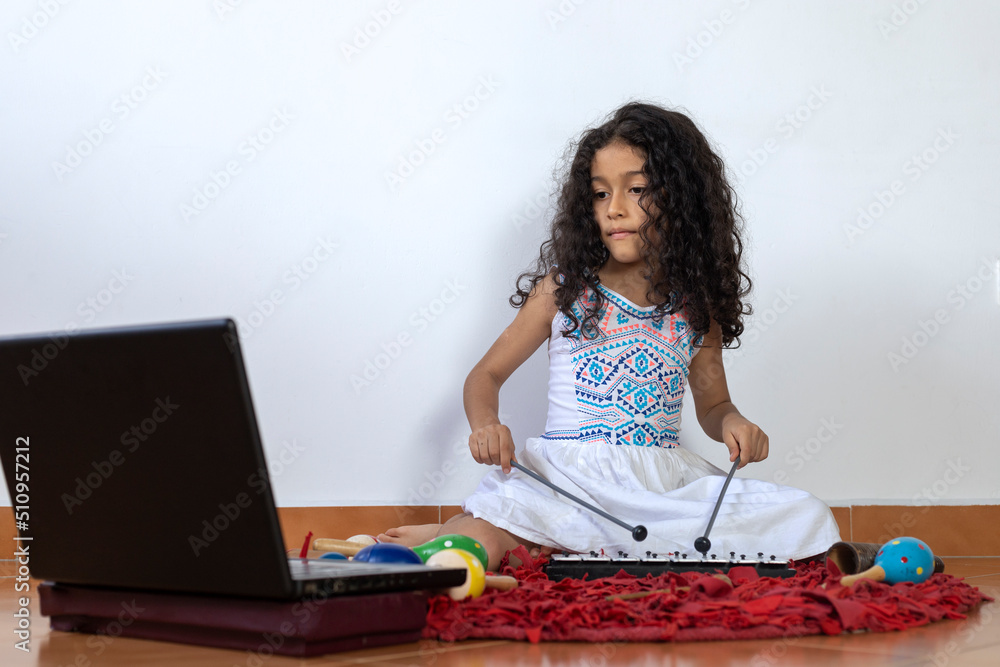 Latin American girl receiving her virtual music class playing a xylophone