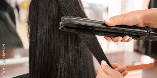 Hairdresser straightening woman's long hair in salon