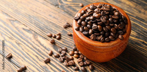 Bowl of roasted coffee beans on wooden background with space for text