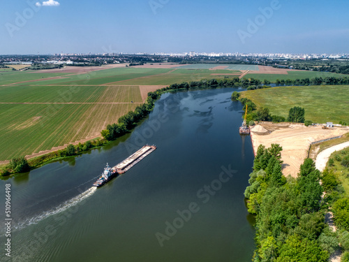 Towboat transports barge with sand along tranquil river