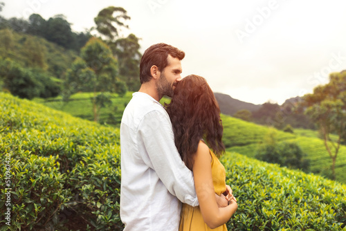 Romantic couple of travelers in love standing against nature background tea plantations landscape. Young adult brunette woman and man in front of perfect natural backdrop near Nuwara Eliya tea farm