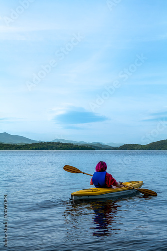 Woman kayaking. Rear view of a young man splashing water while kayaking on the river with mountains background. High-quality photo