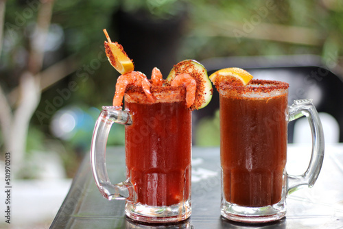 Micheladas served on an outdoor table, it is a Mexican alcoholic drink that is prepared by mixing beer, lemon juice, chili, salt and shrimp decorated with orange slices
 photo