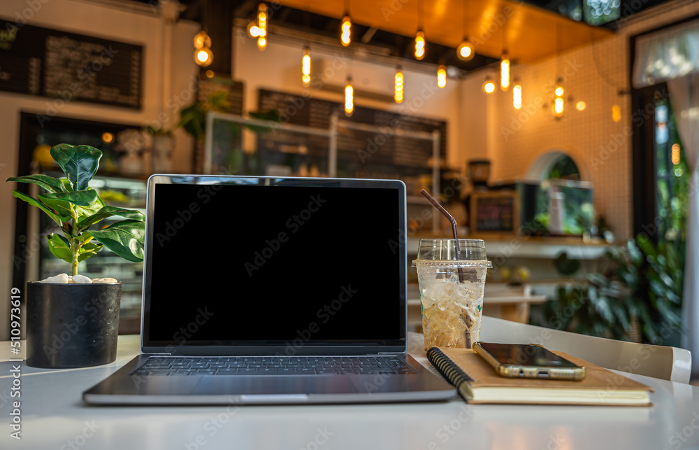 Mockup of laptop computer with empty screen with notebook,ice coffee and smartphone on table side the window in the coffee shop at the cafe,black screen