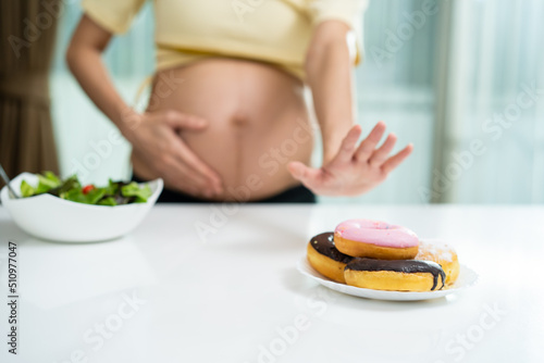 Asian young pregnant woman choose to eat green salad instead of donut.