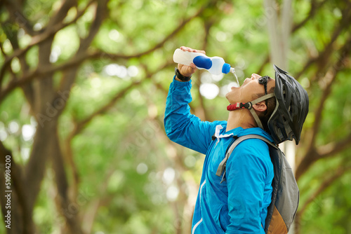Thirsty cyclist in windbreaker, helmet and sunglasses drinking fresh water