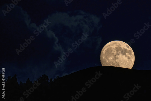 beautiful moonrise over the mountains with tree silhouettes on the horizon photo