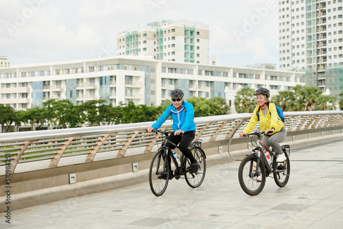 Joyful young Asian man and woman riding bicycles in city park © DragonImages