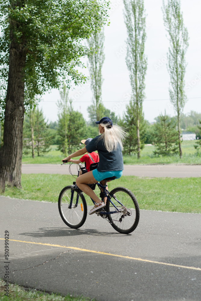 Fototapeta premium a young woman with a child rides a bicycle in a city park on a summer day, side view