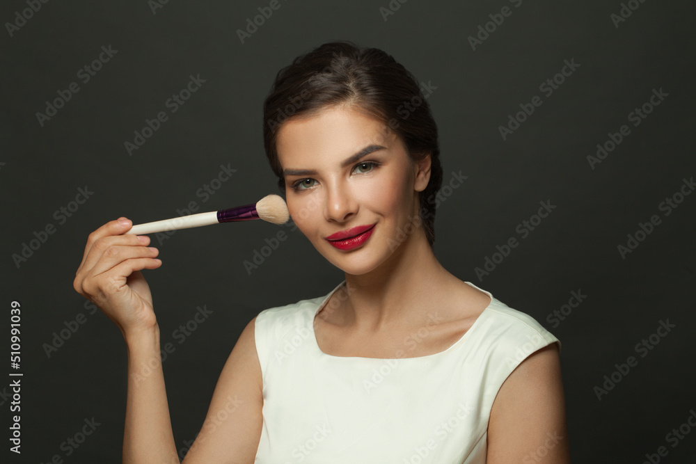 Obraz premium Close up beauty portrait of an attractive lovely young woman holding makeup blusher brush on black