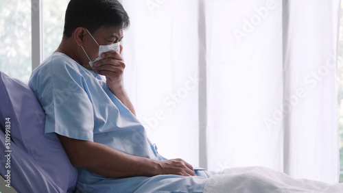 Asian old man is hospitalized with COVID-19. Old male patient wearing a medical mask sits on the patient's bed. © ronnarong