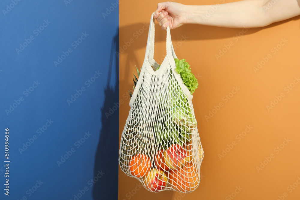 Female hand holds string bag with grocery on two tone background