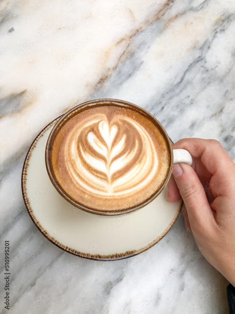 top view hand holding a cup of cappuccino or latte coffee on table top view hand holding a cup of cappuccino or latte coffee on table