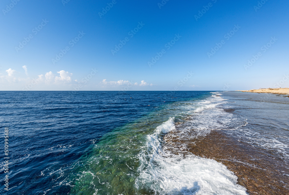 Seascape of the Red Sea in Egypt near Marsa Alam, Africa. A group of people are snorkeling over the coral reef and the waves breaking on the coast.