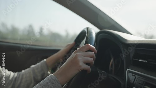 Profile side shot of female hands on steering wheel of private car or vehicle. Driving on highway or country road. Woman's hands driving the car as it goes on the road during sunny day photo