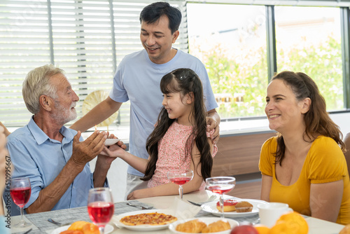 Happy family gathering enjoying having lunch together at home. Child daughter celebration around dining table with parents  grandparents and multi-generation family