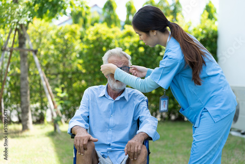 Female nurse with senior man sitting on wheelchair in garden. Caring Asian nurse taking care of old man in wheelchair at the hospital ward. People and health care concept
